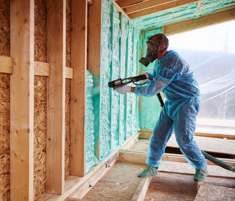 Worker using spray foam insulation in a home